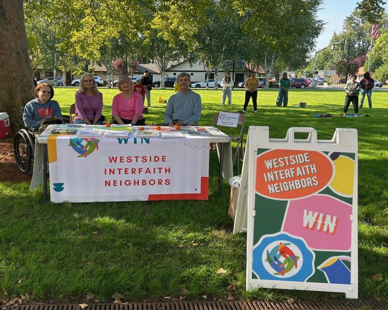 Westside Interfaith Neighbors community table at Welcome Beaverton, with WIN banner and volunteers in a park.